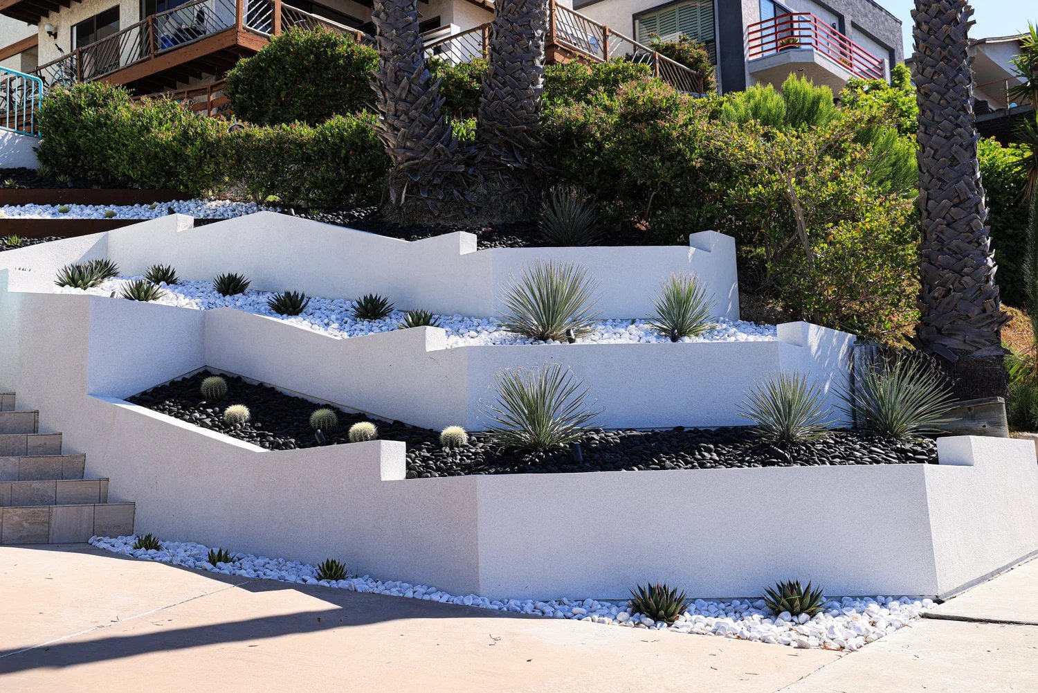 Tiered white stucco retaining walls with black and white stone beds and succulent plantings