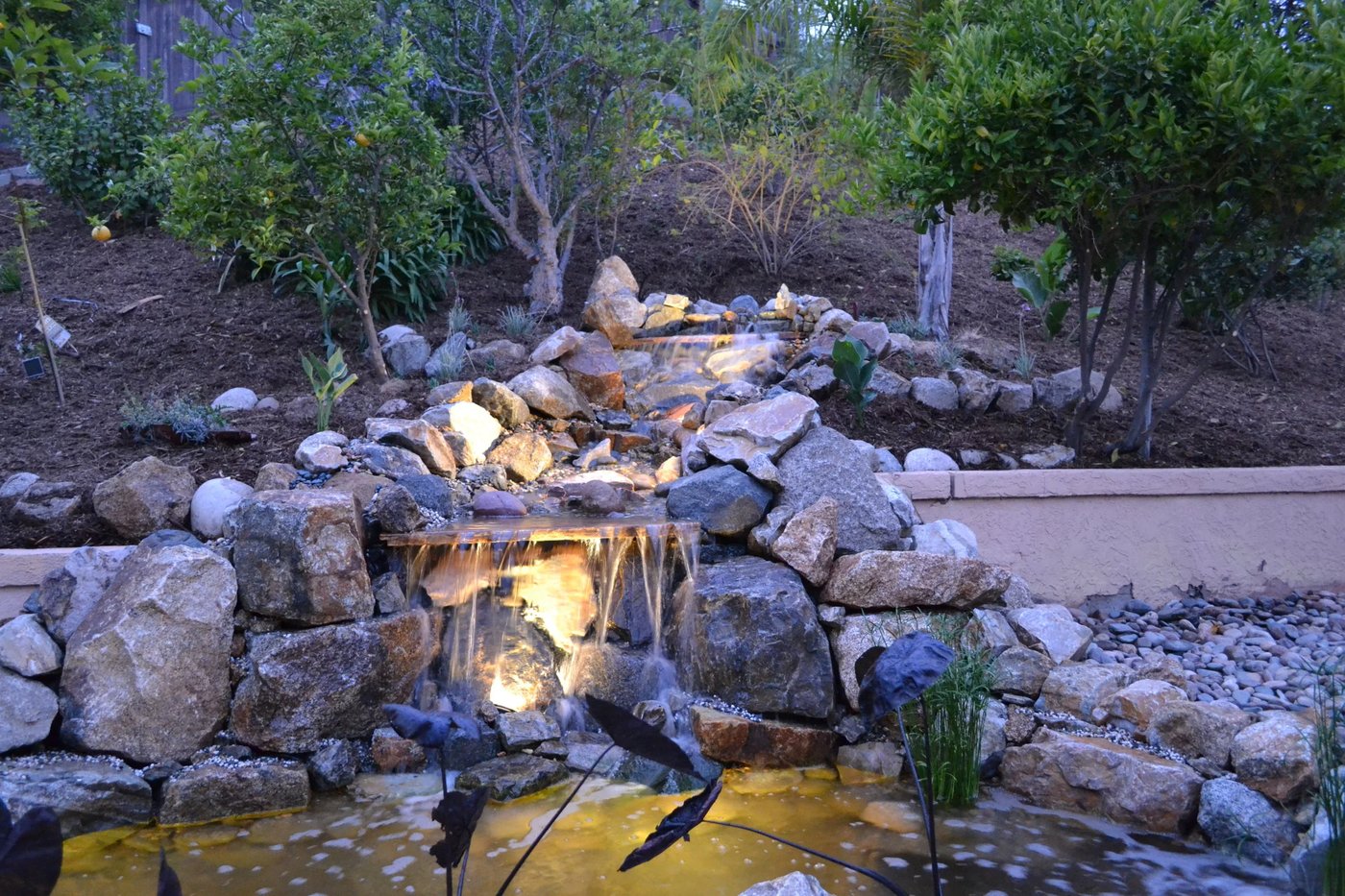 Custom stacked-stone waterfall feature illuminated at dusk